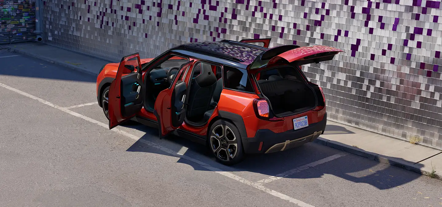 Rear top view of the all-electric MINI Aceman in Rebel Red and Black Roof with open doors on a street.