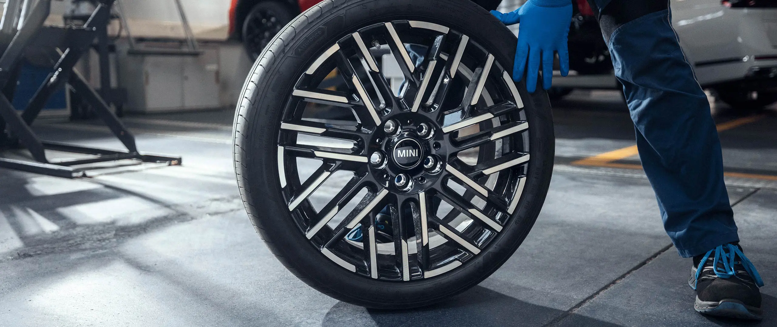 A MINI Partner service technician rolls an 18" Night Flash Spoke Bicolour Light Alloy Wheel into position.