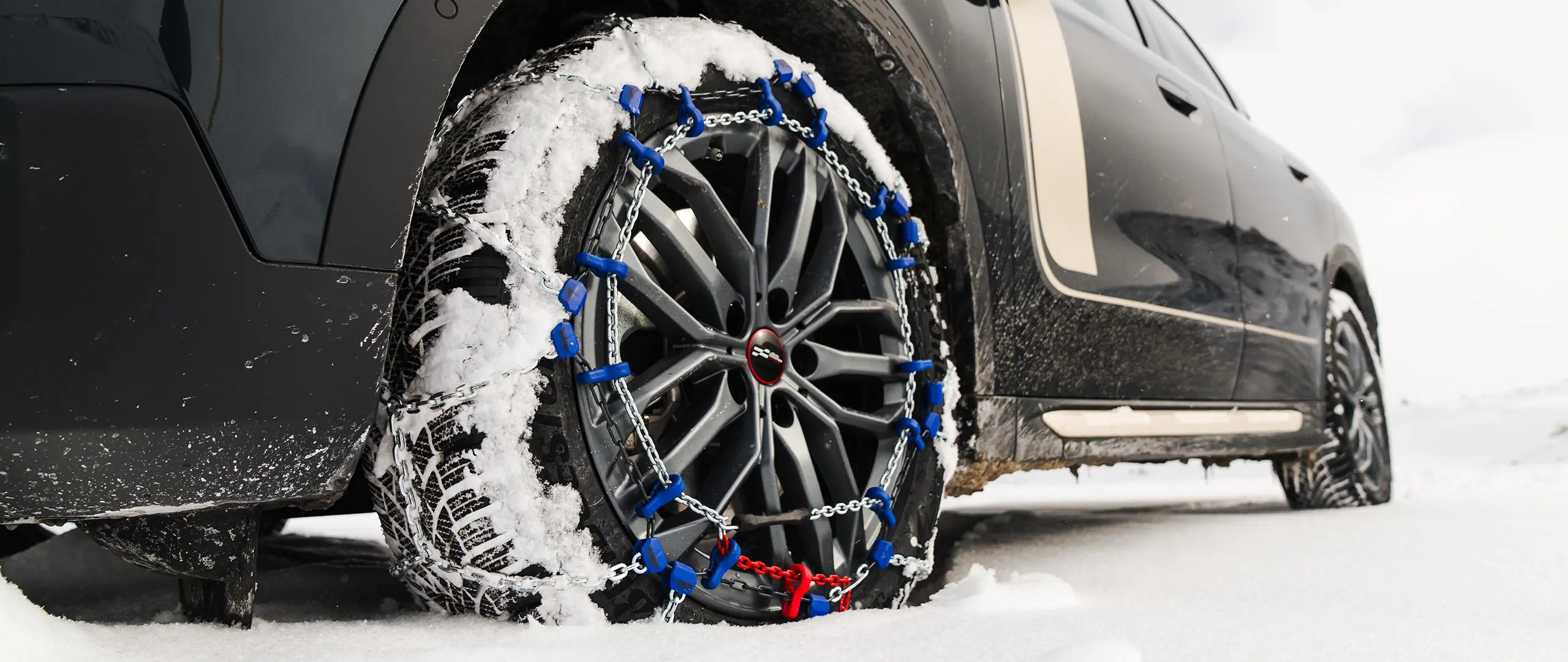 Close-up of a tyre chain installed on the wheel of a MINI Countryman for extra traction as it drives through heavy snow. 