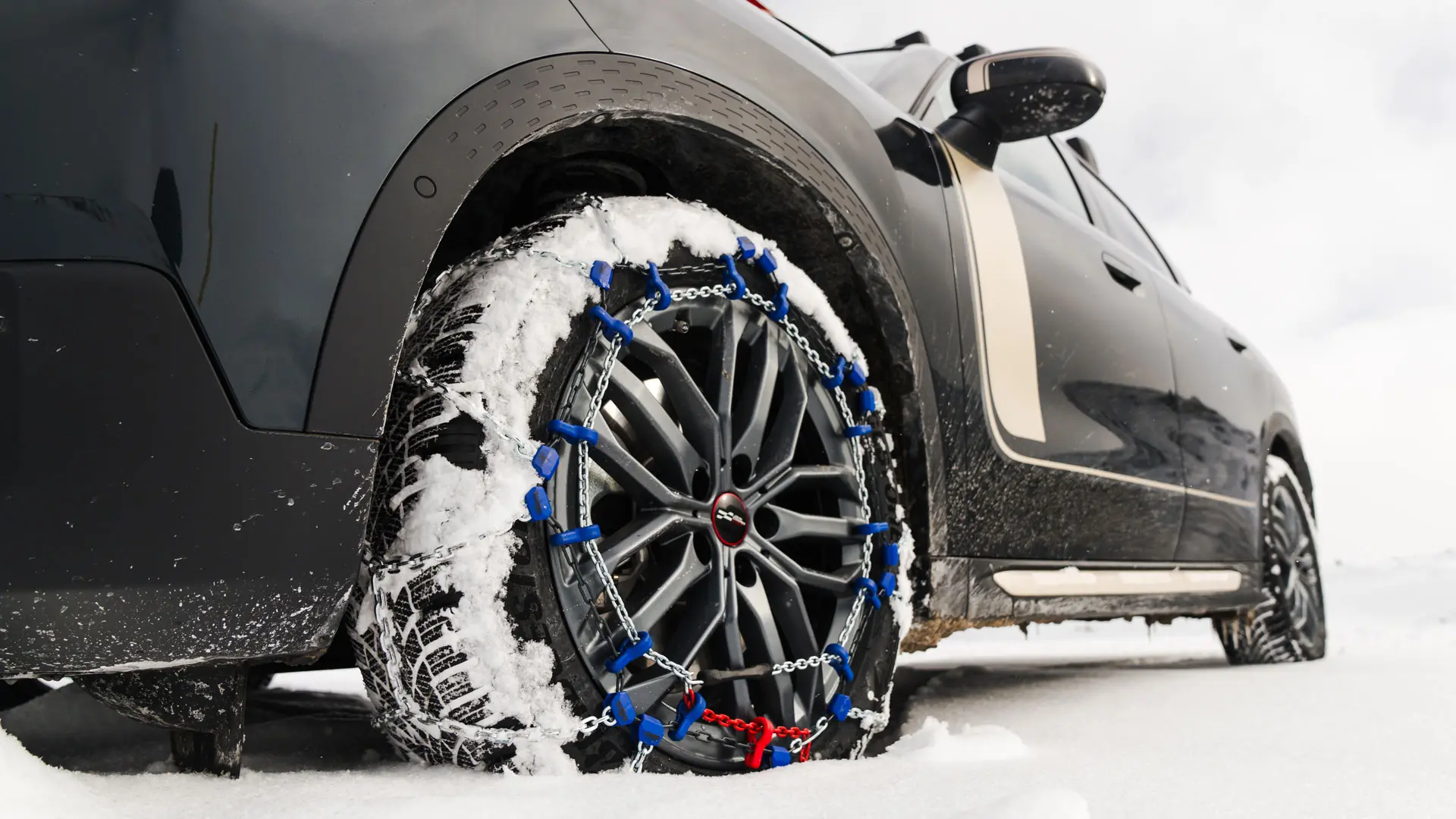 Close-up of a tyre chain installed on the wheel of a MINI Countryman for extra traction as it drives through heavy snow. 