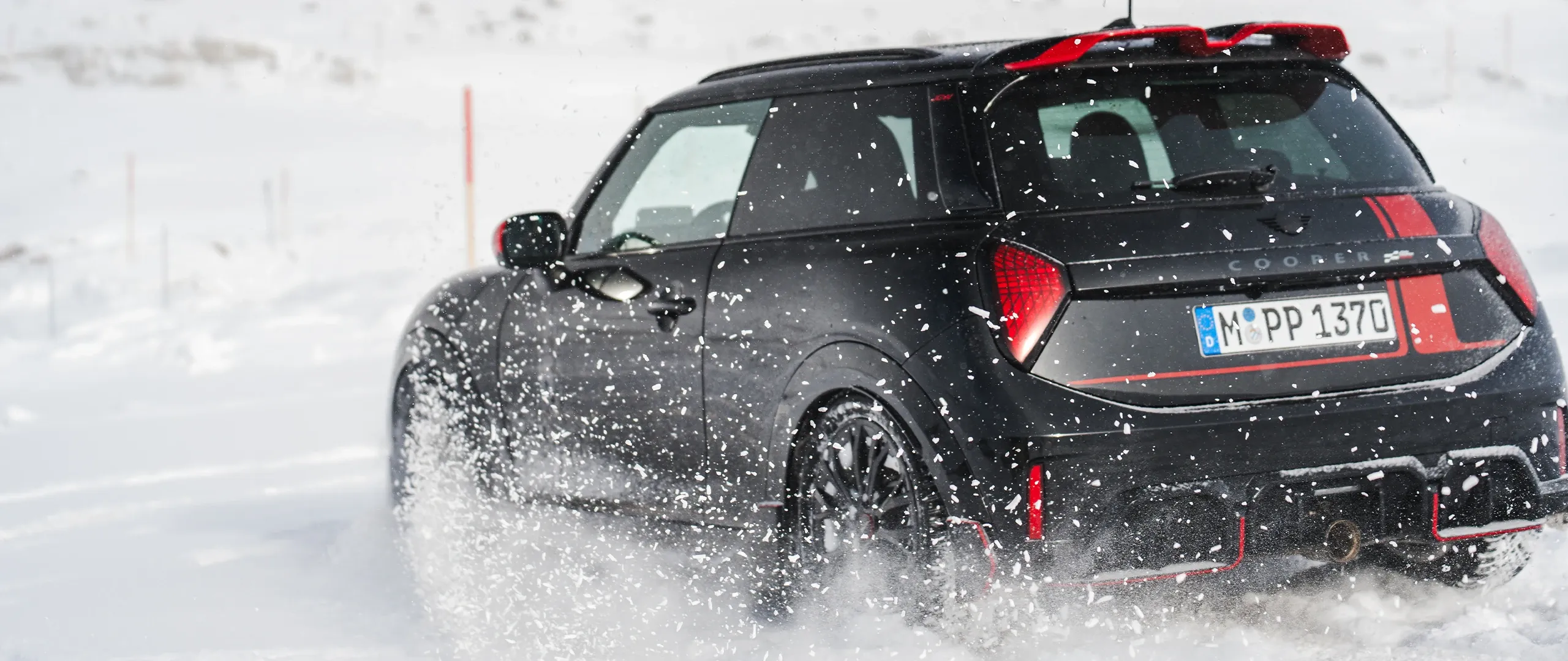 Rear view of a MINI Cooper JCW driving through the snow.