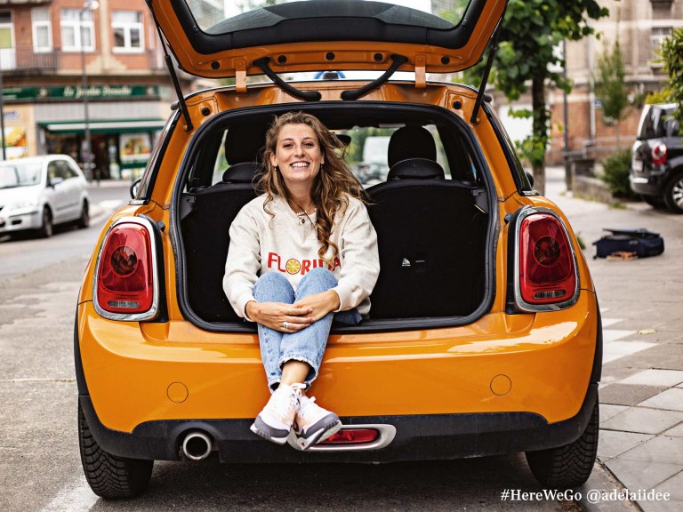MINI 3-door hatch in volcanic orange with happy woman sitting in trunk